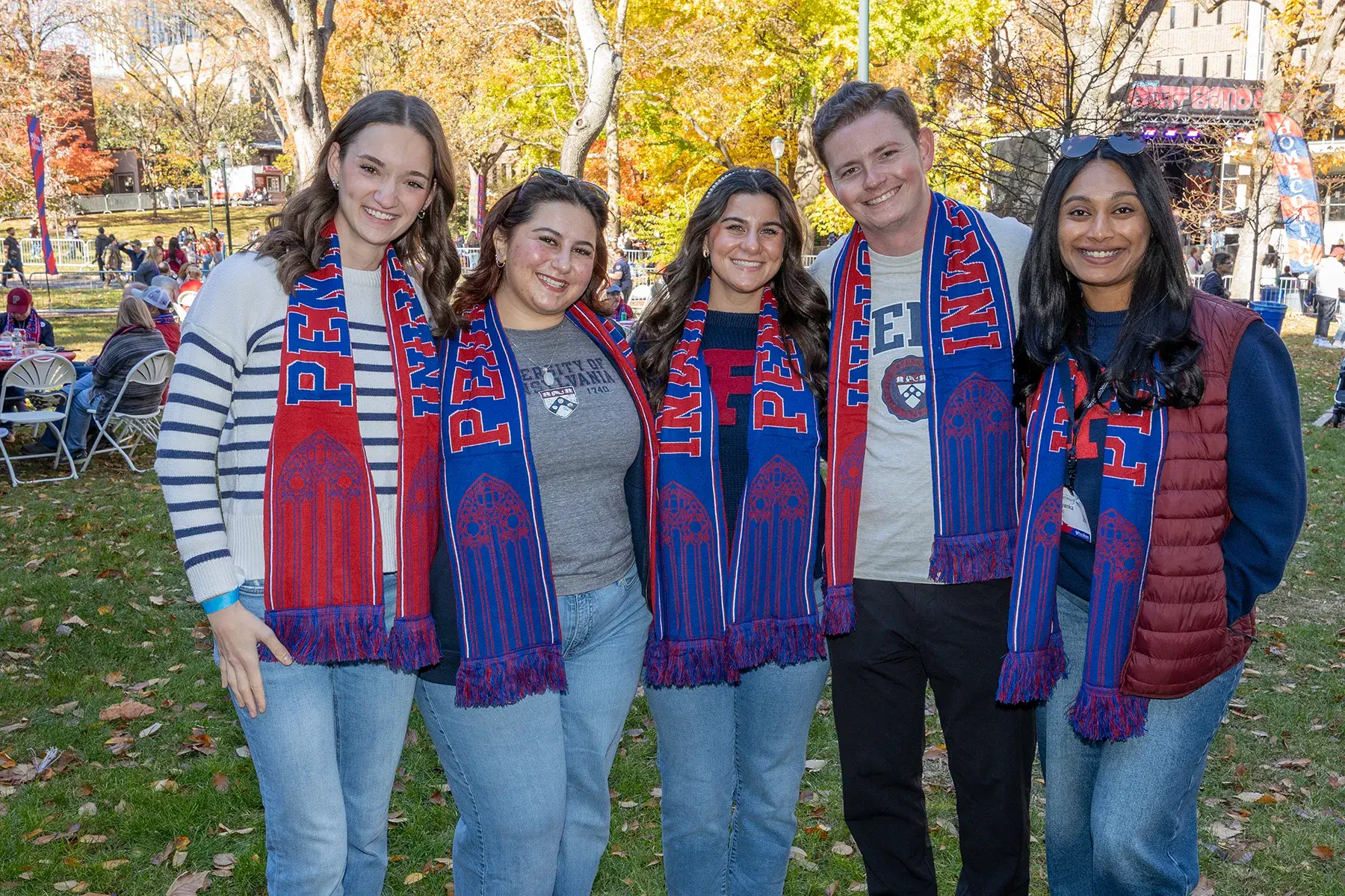 Five Penn community members wearing red and blue scarves pose together outdoors during Homecoming Weekend 2025.