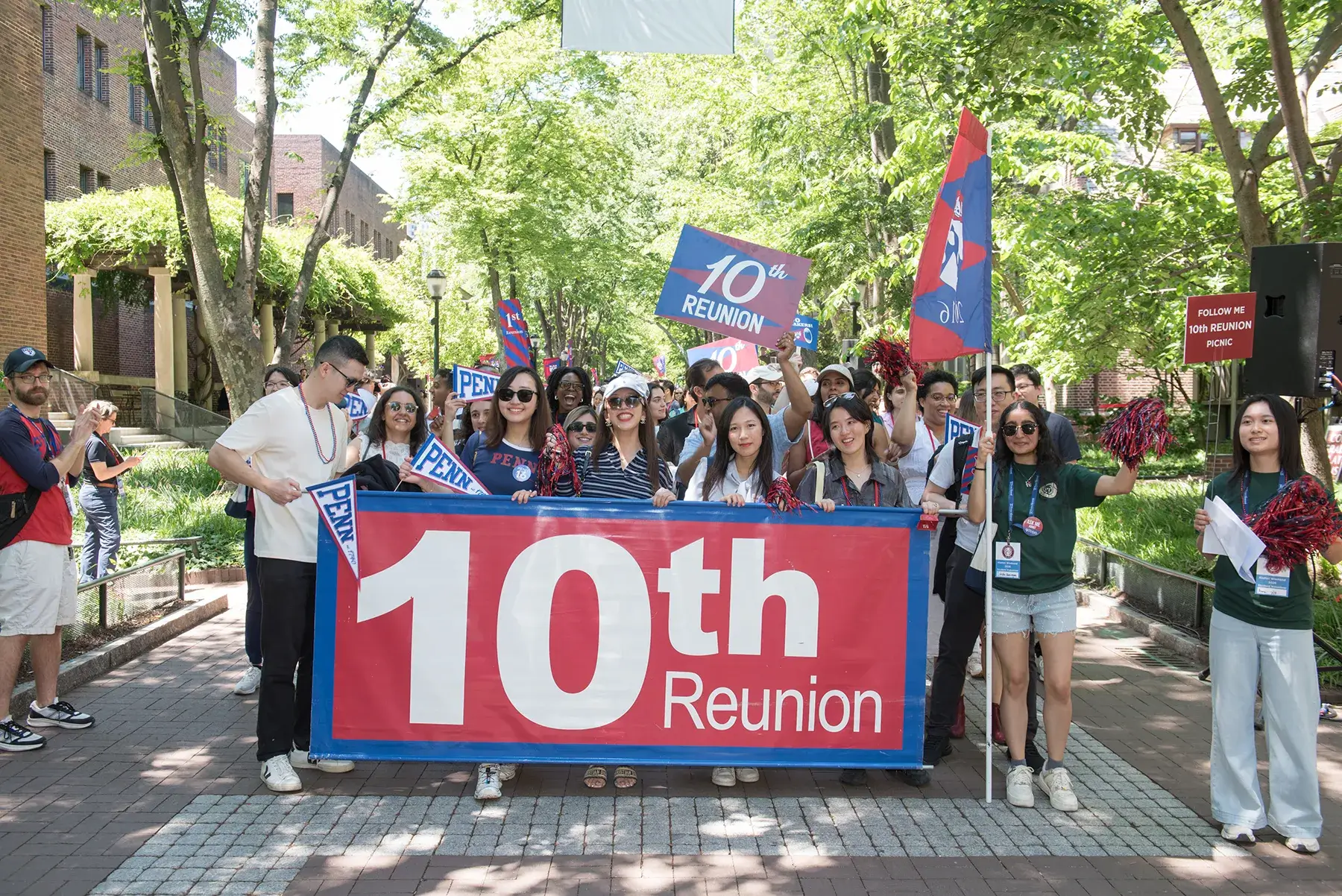 A large group of Penn alumni poses with a “10th Reunion” banner, pennants, and pom-poms during Alumni Weekend 2026.