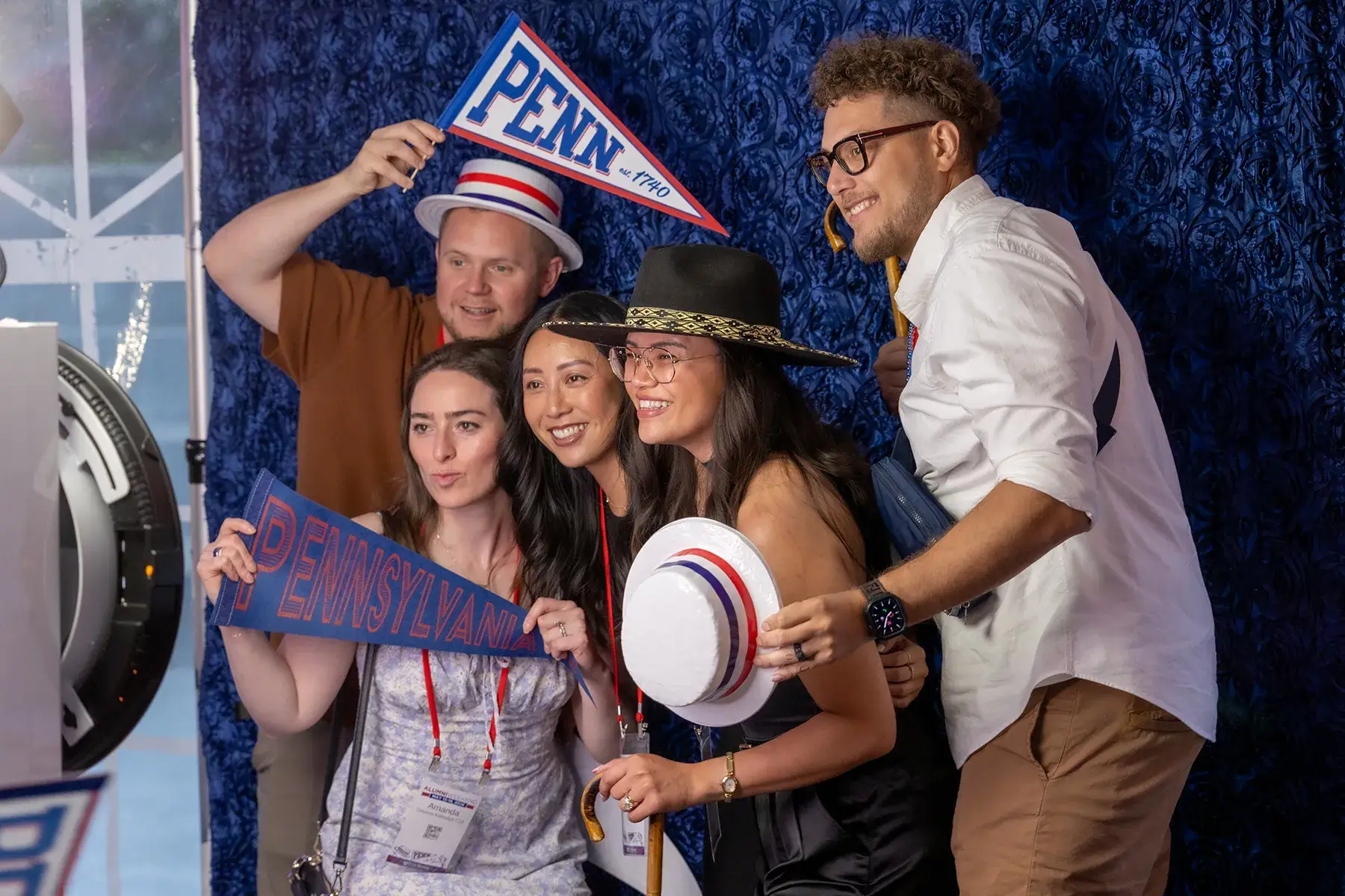 Five Penn alumni pose with hats and school pennants in a photo booth during Alumni Weekend 2026.