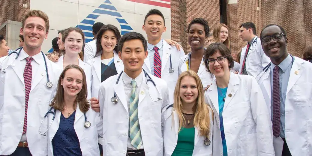 A group of Penn Medicine students wearing white coats and stethoscopes smile together outdoors.