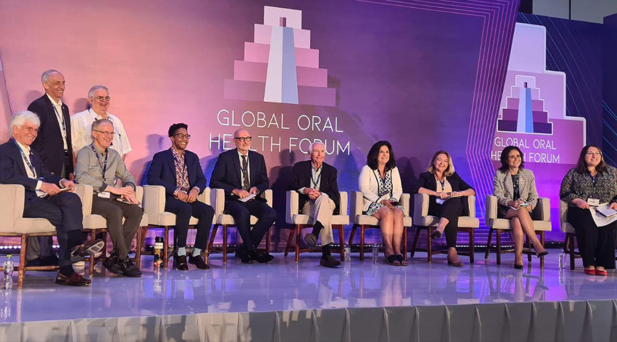 A group of eleven dental health professionals sit together on stage at the Global Oral Health Forum