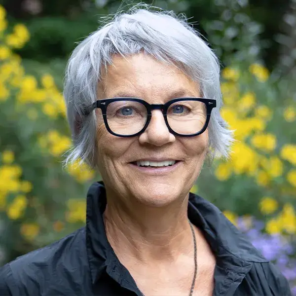 Headshot of Doris Wagner wearing black glasses, photographed outdoors with yellow flowers in the background.