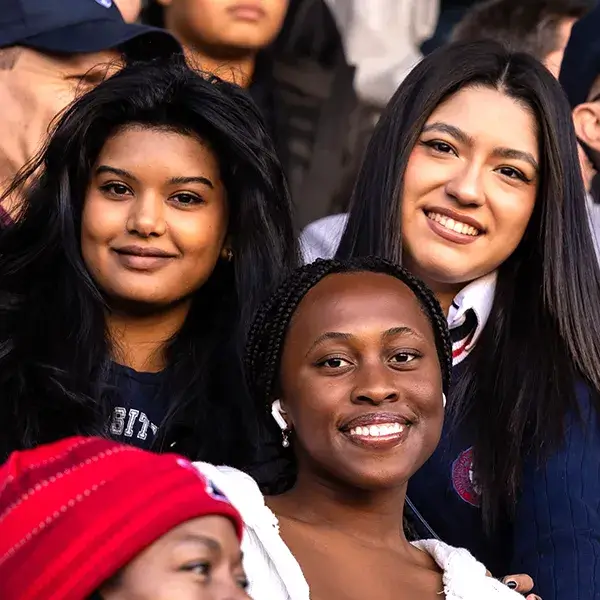 Penn alumni and students cheer from the stands during a homecoming football game, showing spirited engagement and Quaker pride.