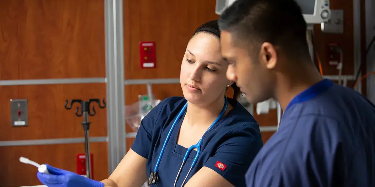 Two nursing students in scrubs review clinical information in a simulation lab.