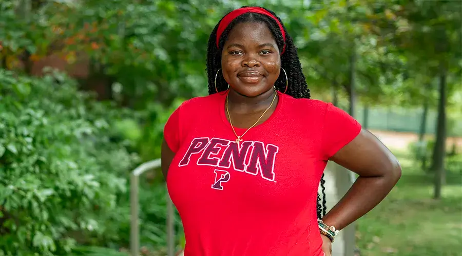 Herinah Asaah, C’26, standing outdoors in a red Penn shirt