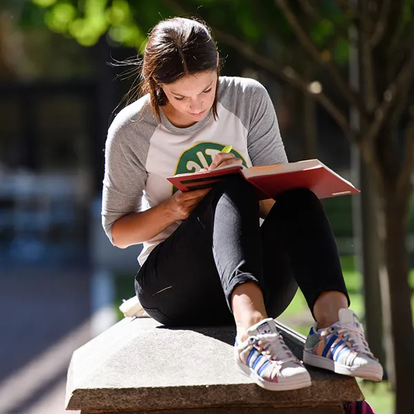 A Penn student sits in a courtyard writing in a notebook.