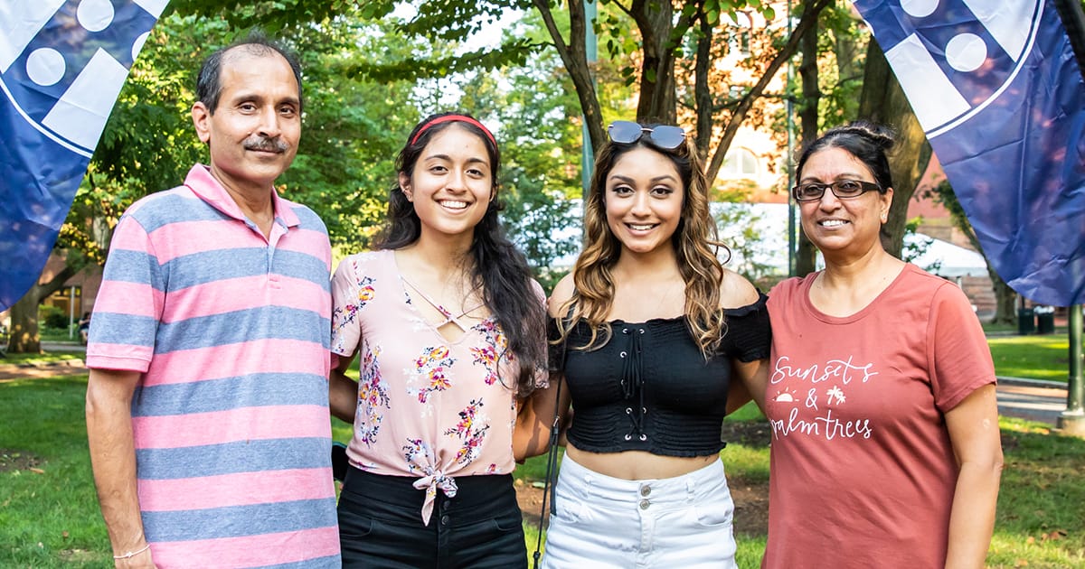 Two Penn students stand on College Green flanked by their parents