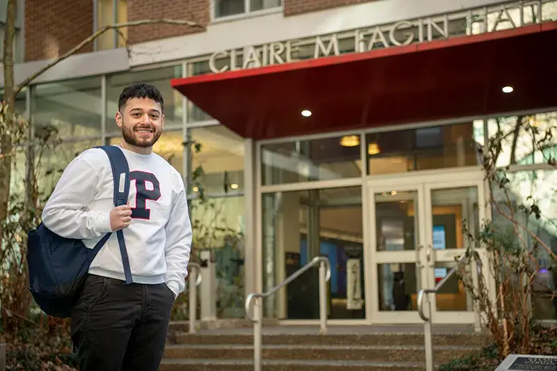 Penn student in a white sweatshirt stands confidently in front of Fagin Hall.