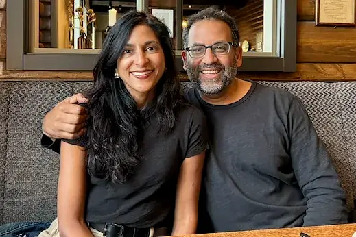 Sapna and Ashish Shah seated together at a restaurant, smiling at the camera