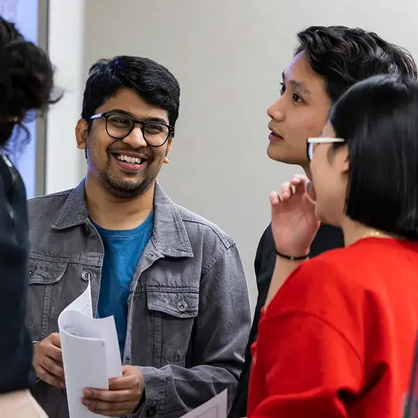 A group of students from Penn's School of Social Policy and Practice engaged in conversation, holding papers and smiling.