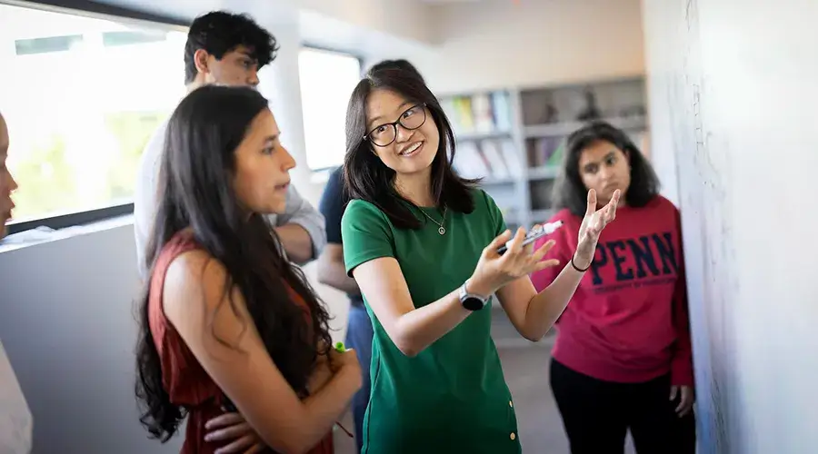 Graduate students gather around a whiteboard, discussing ideas in a classroom setting at the University of Pennsylvania.